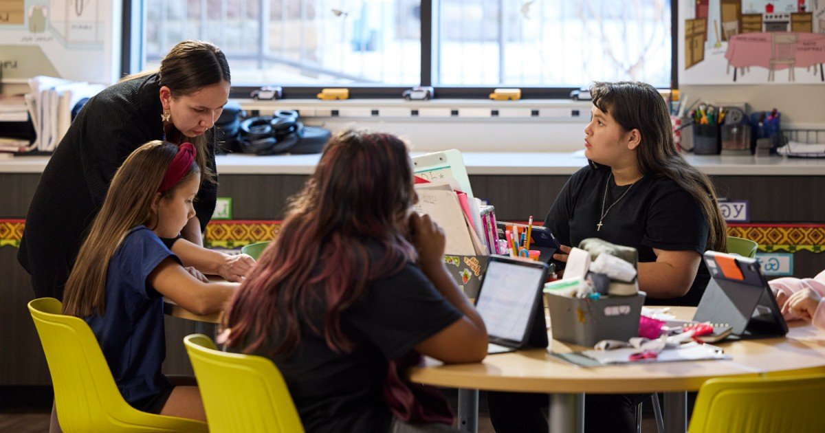 Elder teaching younger person Cherokee language on an iPad, with a Mac in the background.