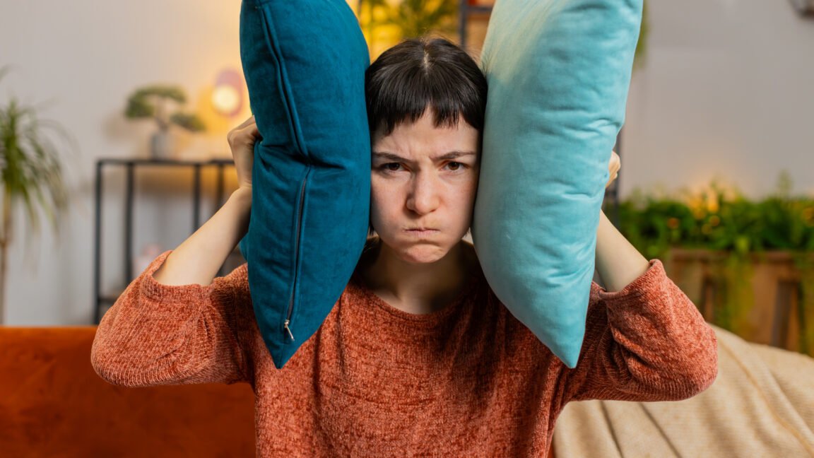 A person covering their ears in frustration while watching a streaming service on a TV, symbolizing the annoyance of loud ads.