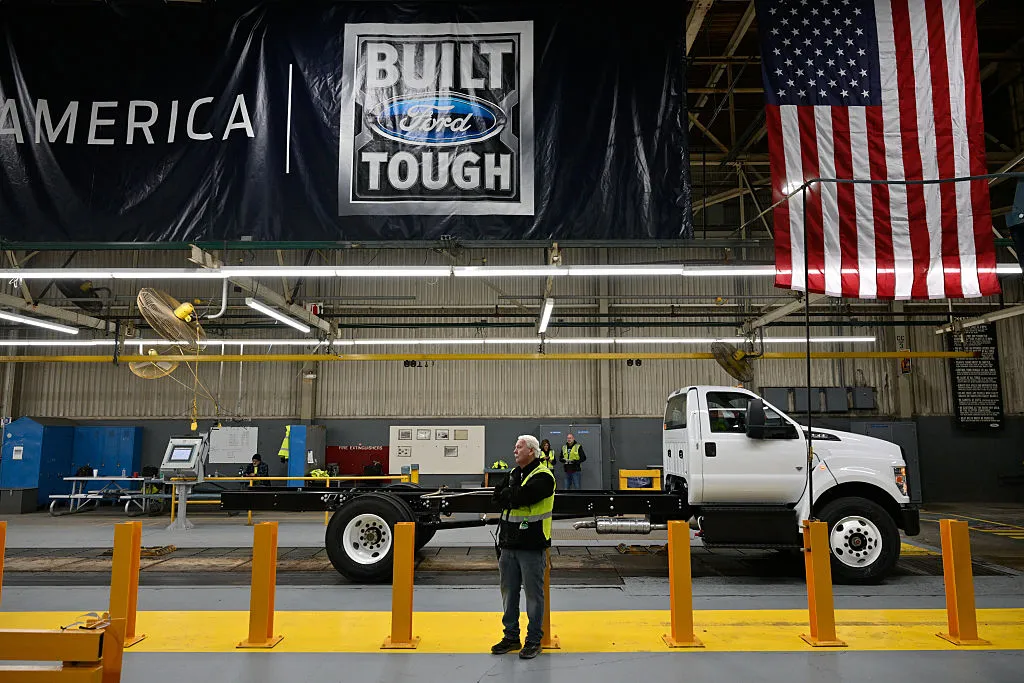 Ford engineers working on a car engine, symbolizing the company rehiring experienced staff.