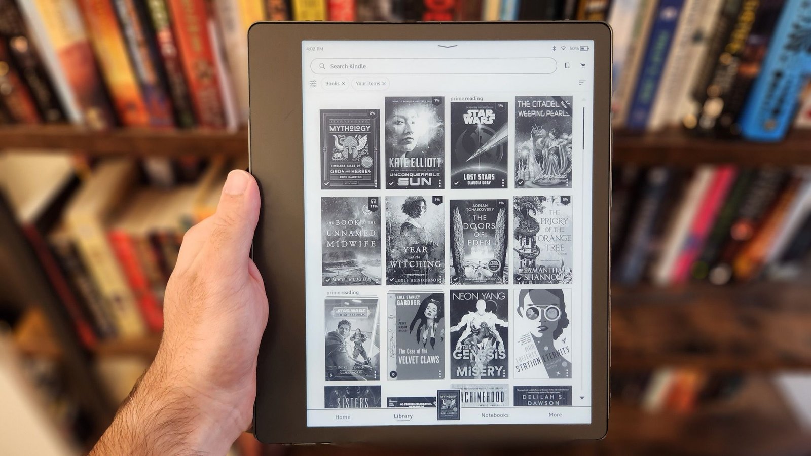 Amazon Kindle Paperwhite e-reader displaying a book cover, with a stack of other Kindles in the background.